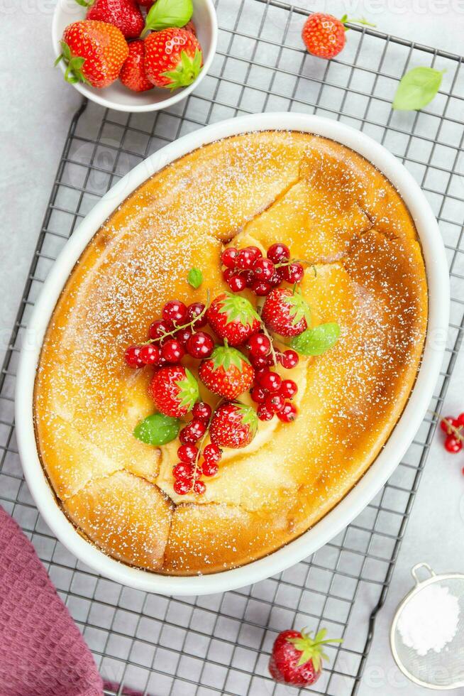 Homemade casserole with cottage cheese, semolina, fresh red currant berries and strawberry on light gray background. Top view. Close up. photo