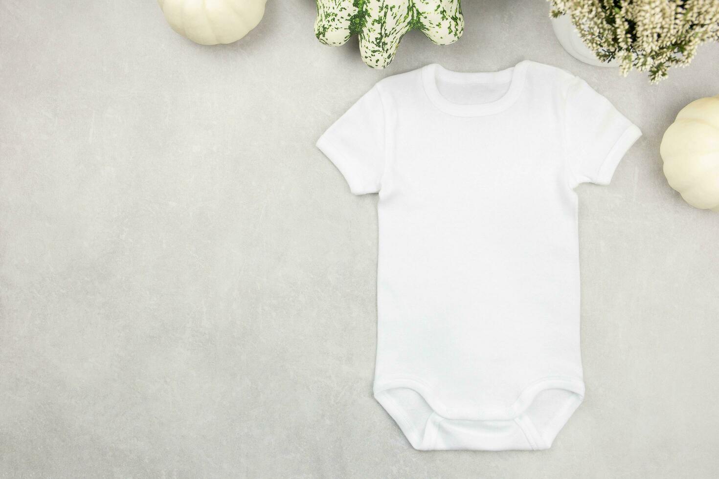 White baby girl or boy bodysuit mockup flat lay with pumpkins on gray concrete background. Design onesie template, print presentation mock up. Top view. photo