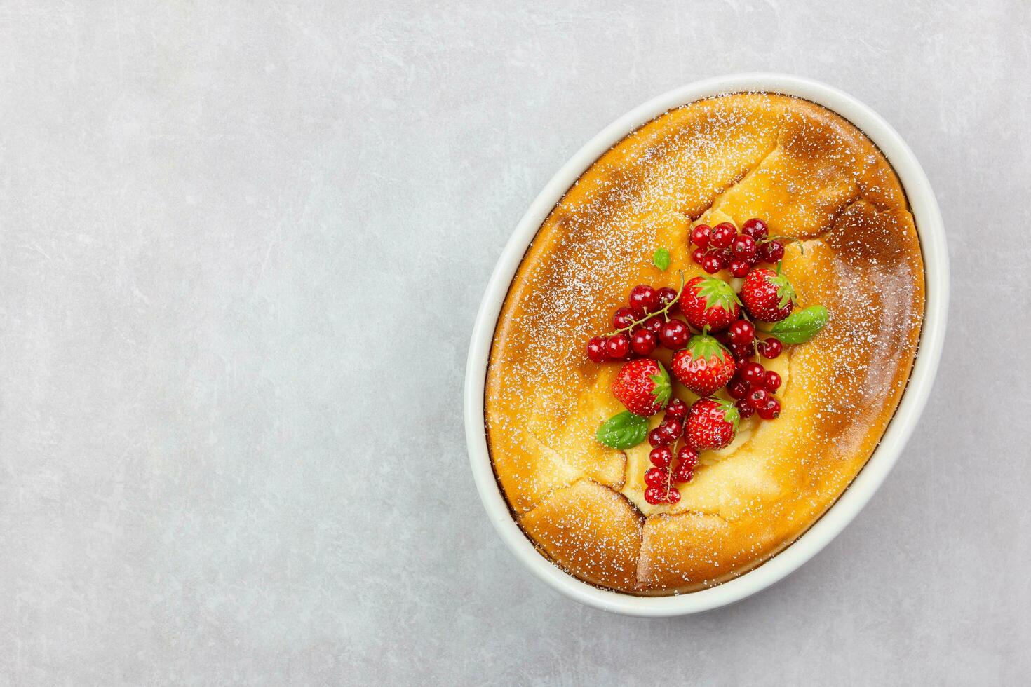 Homemade casserole with cottage cheese, semolina, fresh red currant berries and strawberry on light gray background. Top view. Copy space. photo