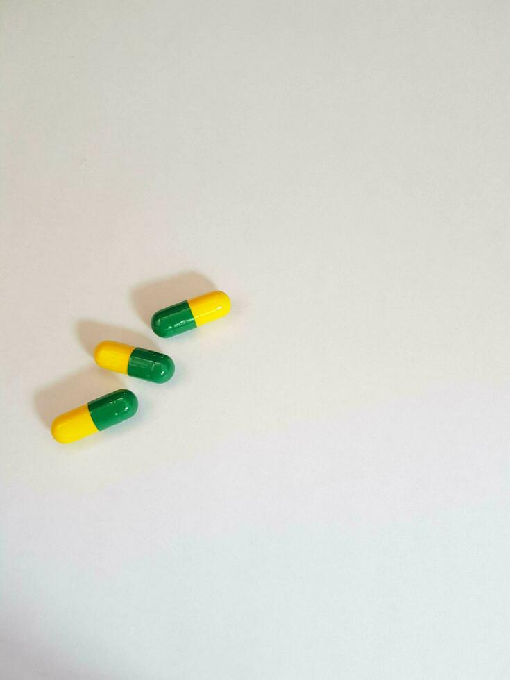Isolated white photo of three medicine capsules green and yellow.