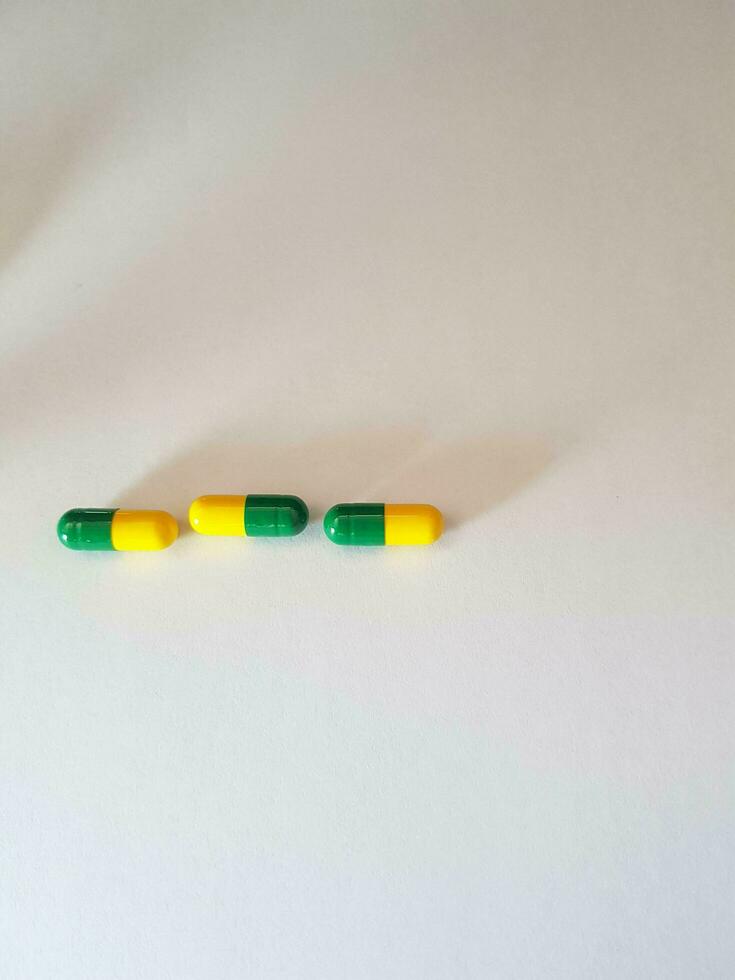 Isolated white photo of three medicine capsules green and yellow.