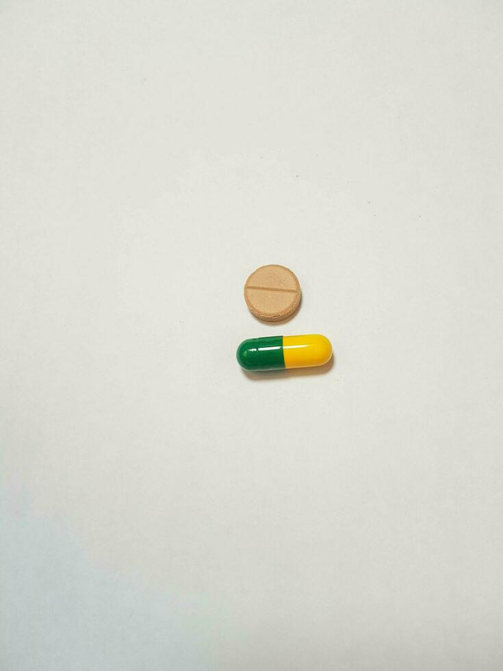 isolated white photo of a brown tablet and a green and yellow capsule