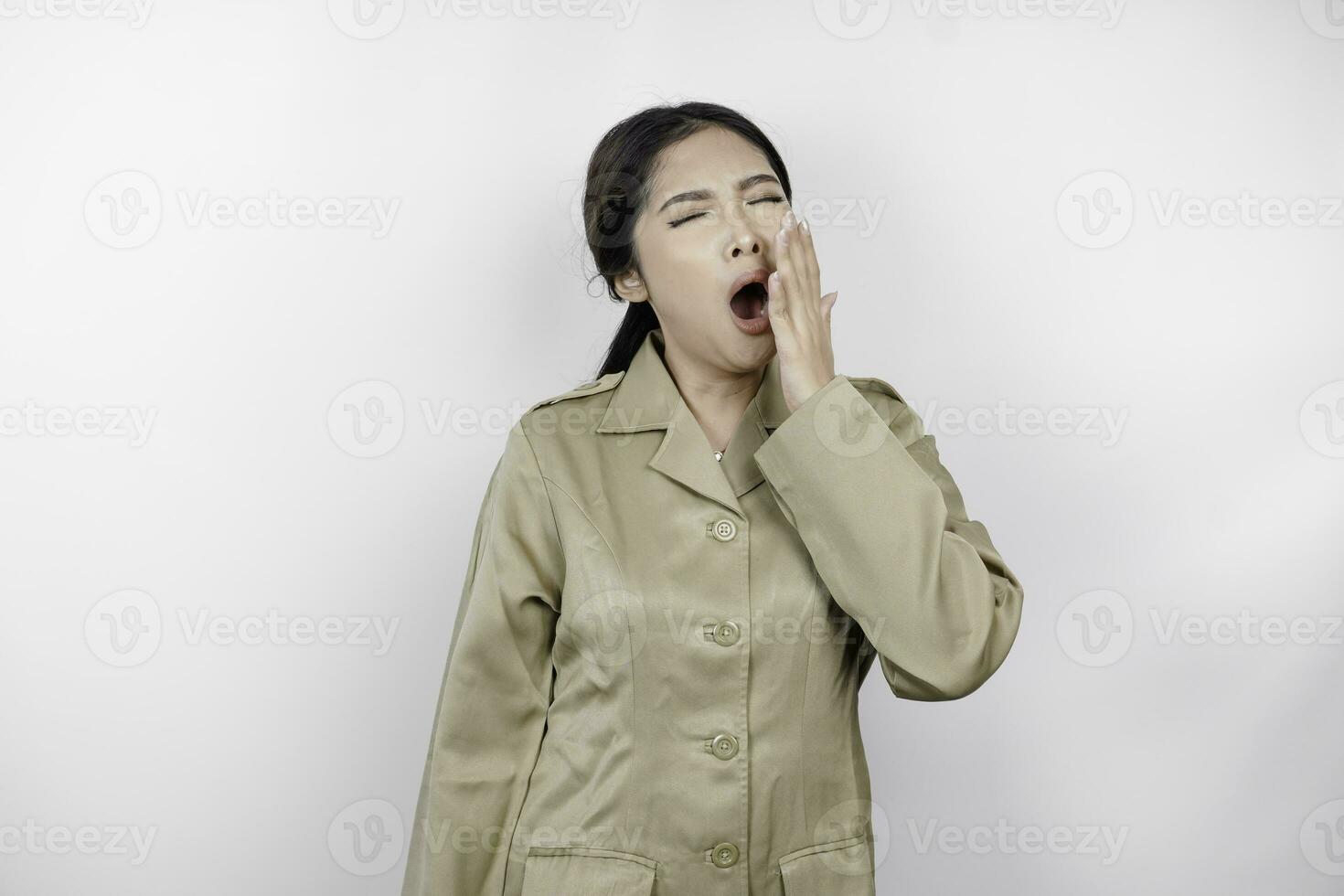 retrato de soñoliento asiático mujer vistiendo un marrón uniforme y cubierta su boca con un mano mientras bostezando aislado imagen en blanco antecedentes foto