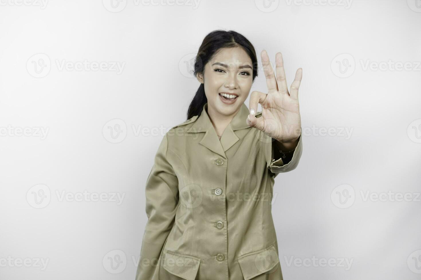 A young Asian woman in brown khaki uniform showing OK sign with her fingers. Indonesian government worker. photo