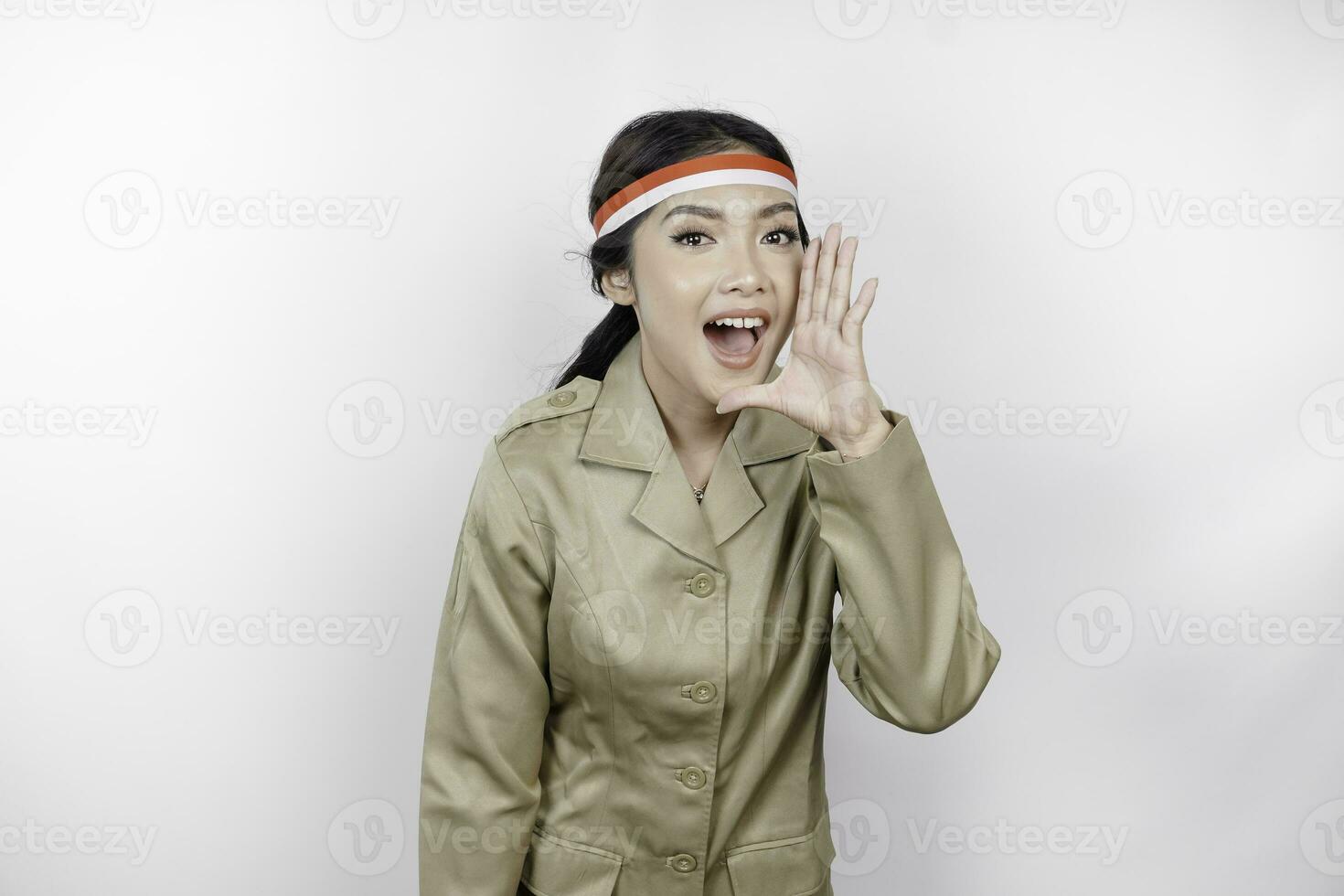 Young beautiful civil worker woman is wearing indonesia's flag headband and shouting or yelling isolated by a white background. Communication and independence day concept photo