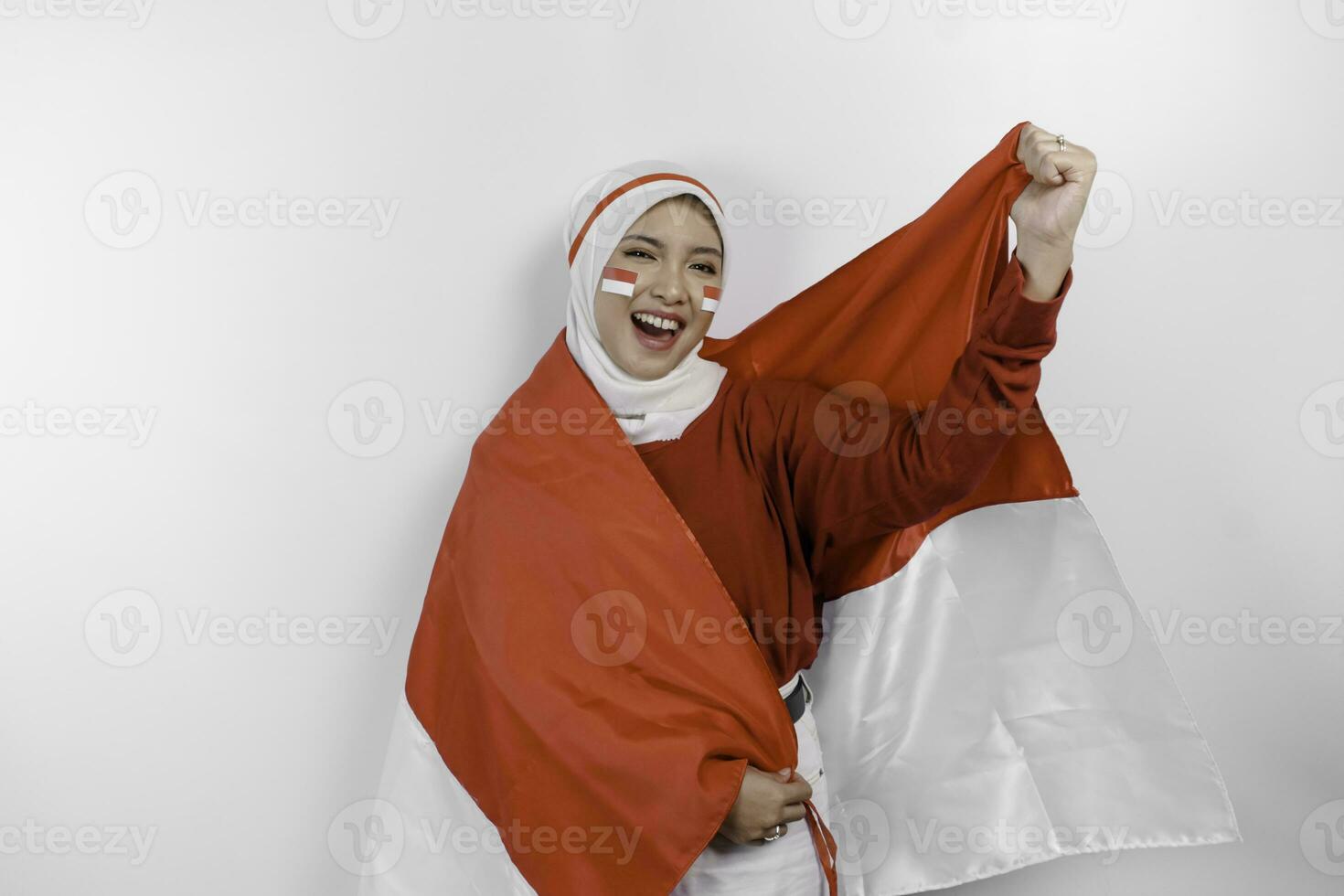 A young Asian muslim woman with a happy successful expression wearing red top and white hijab while holding Indonesia's flag, isolated by white background. Indonesia's independence day concept. photo