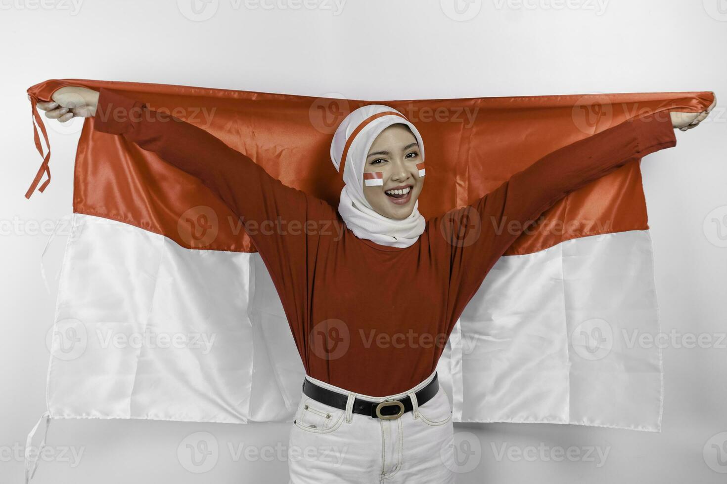 Happy smiling Indonesian muslim woman wearing red top and white hijab holding Indonesia's flag to celebrate Indonesia Independence Day. Isolated by white background. photo