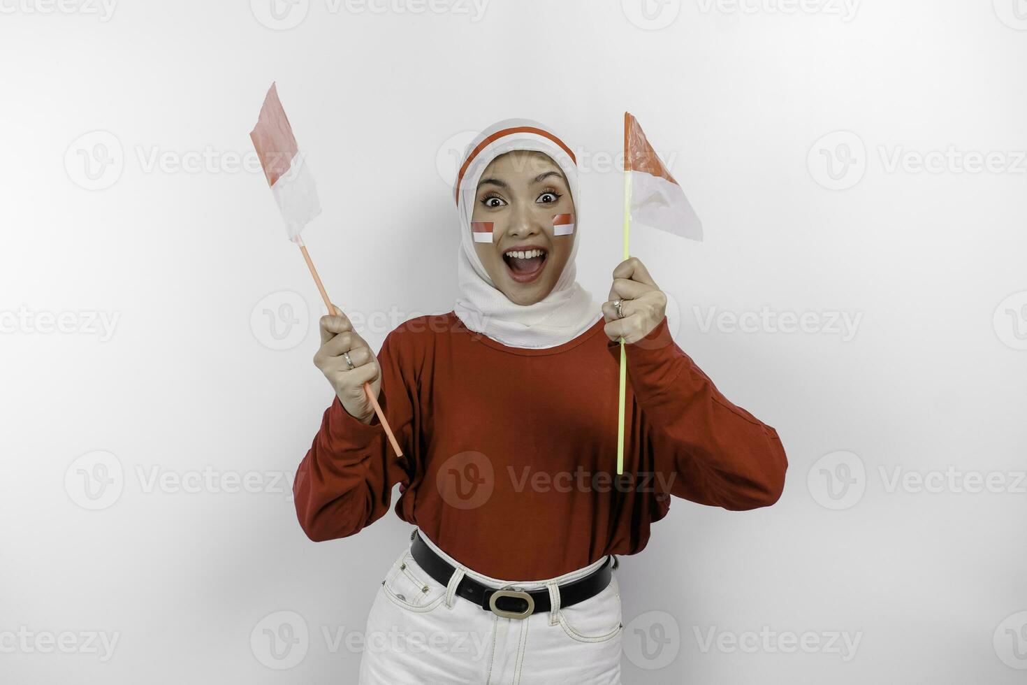 A young Asian muslim woman with a happy successful expression wearing red top and white hijab while holding Indonesia's flag, isolated by white background. Indonesia's independence day concept. photo