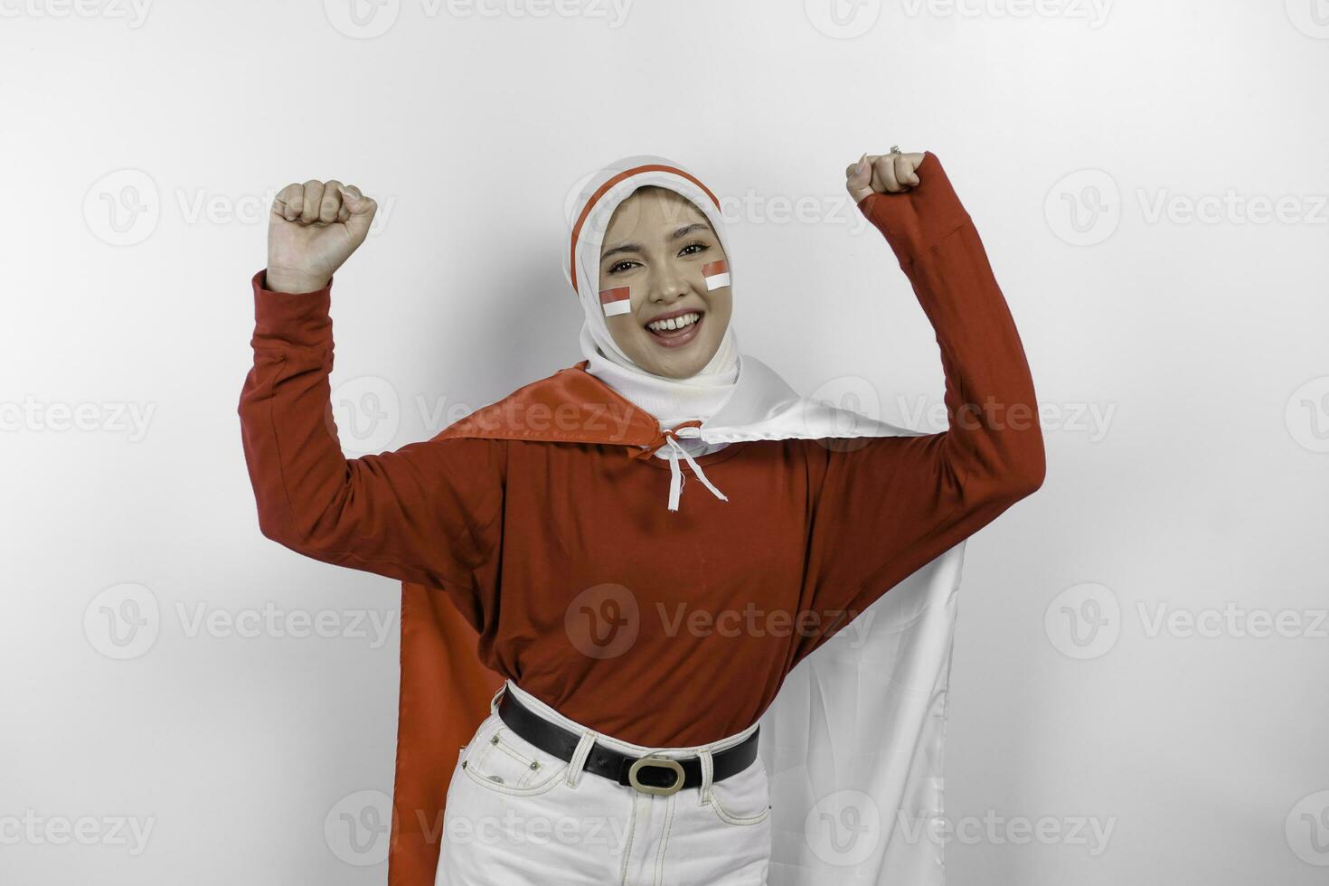 A young Asian muslim woman with a happy successful expression wearing red top and white hijab while holding Indonesia's flag, isolated by white background. Indonesia's independence day concept. photo