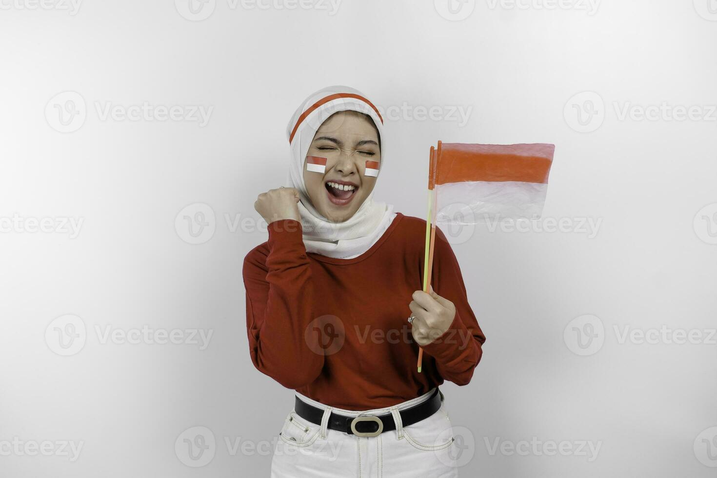 A young Asian muslim woman with a happy successful expression wearing red top and white hijab while holding Indonesia's flag, isolated by white background. Indonesia's independence day concept. photo