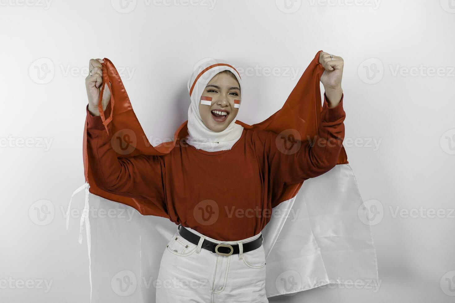 A young Asian muslim woman with a happy successful expression wearing red top and white hijab while holding Indonesia's flag, isolated by white background. Indonesia's independence day concept. photo