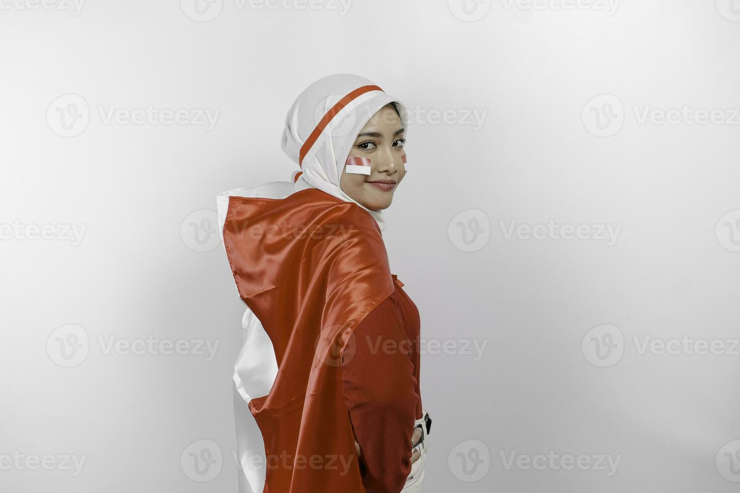 Happy smiling Indonesian muslim woman wearing red top and white hijab holding Indonesia's flag to celebrate Indonesia Independence Day. Isolated by white background. photo