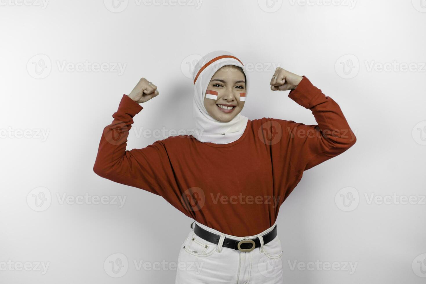 Excited Asian muslim woman wearing a red top and white hijab showing strong gesture by lifting her arms and muscles smiling proudly. Indonesia's independence day concept. photo