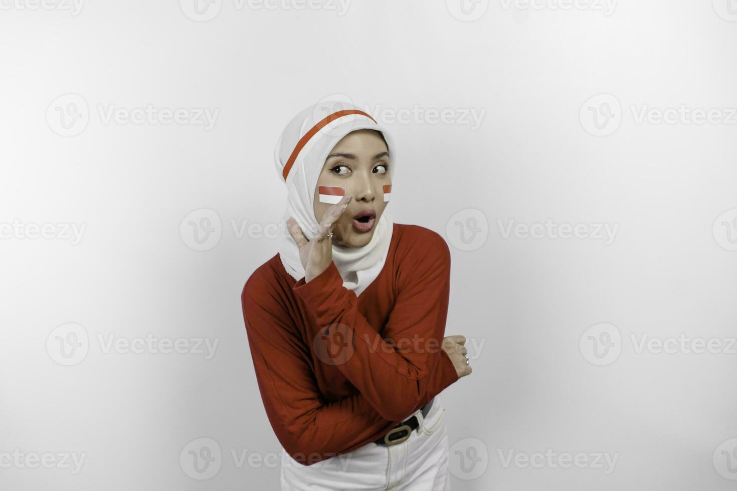 Young beautiful muslim woman wearing a red top and white hijab is shouting and screaming loud with a hand on her mouth. Indonesia's independence day concept. photo