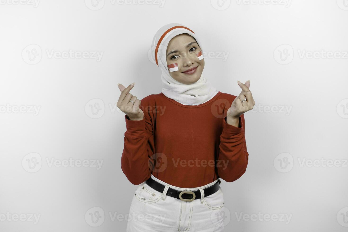 un joven asiático mujer vistiendo un rojo parte superior y blanco hijab siente nacionalismo, formas corazón gesto expresa su amor para Indonesia. de indonesia independencia día concepto. foto