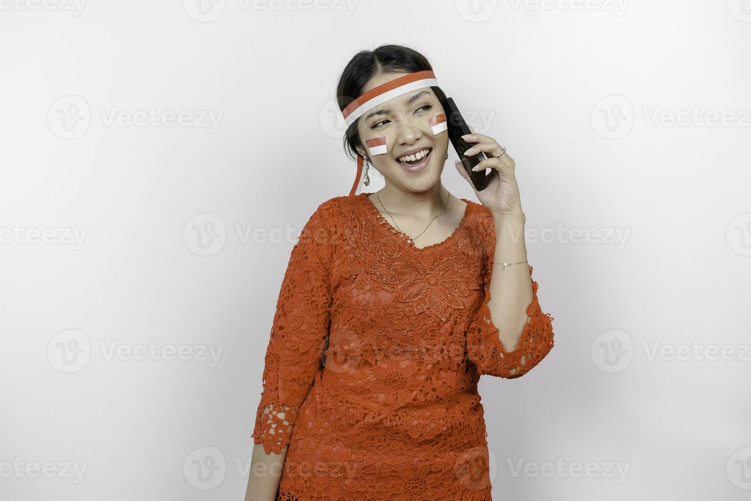 un retrato de un sonriente asiático mujer vistiendo rojo kebaya y venda y participación su teléfono, aislado por blanco antecedentes. de indonesia independencia día concepto foto