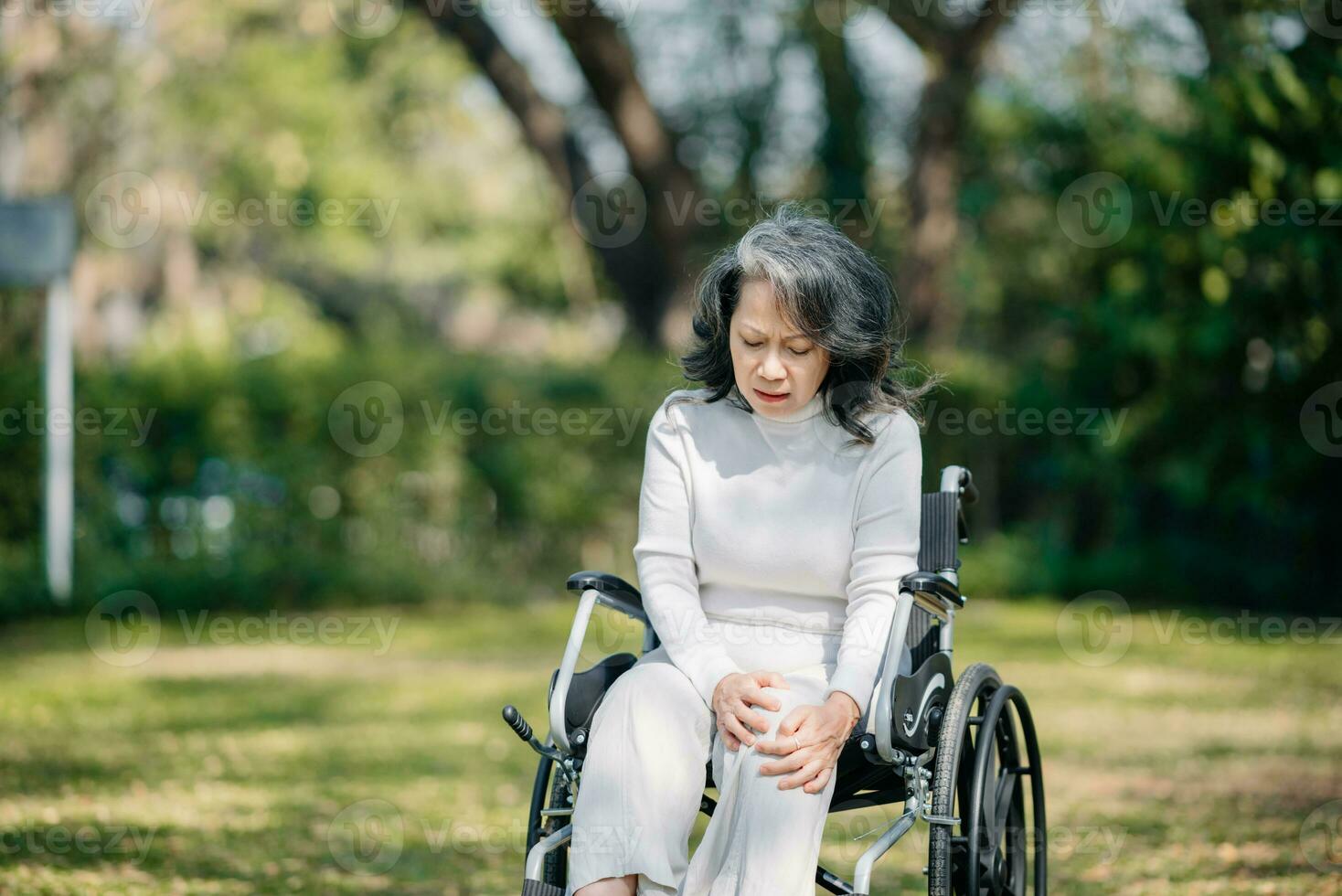 Asian old woman sitting on a wheelchair outdoors in the garden There is pain in the heart photo