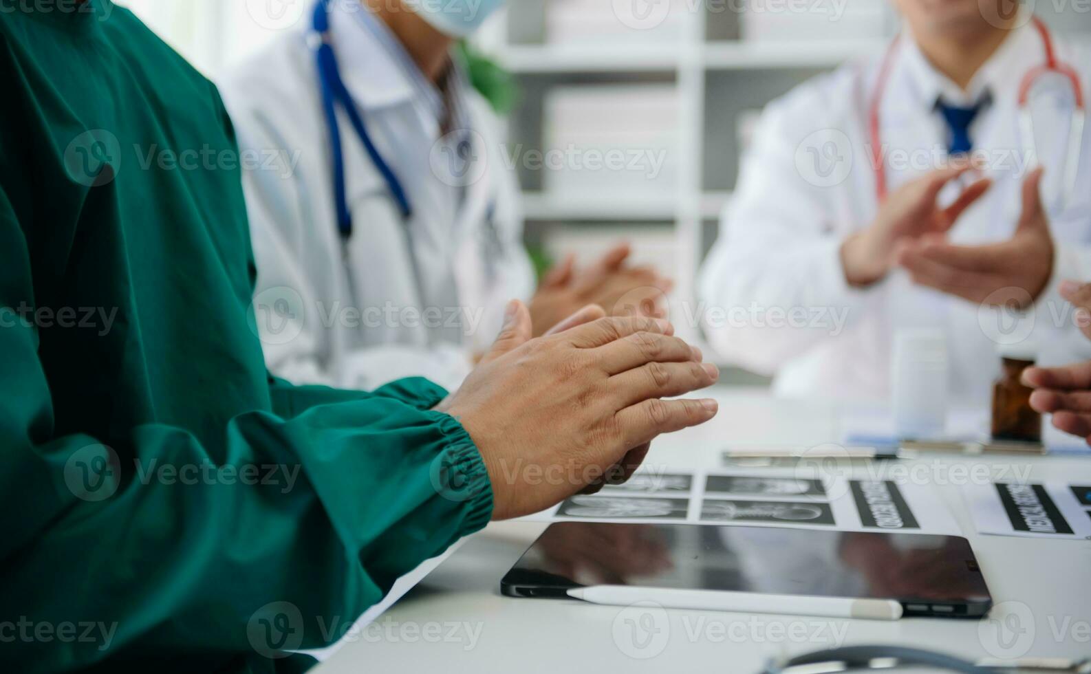 Medical team having a meeting with doctors in white lab coats and surgical scrubs seated at a table discussing a patients working online using computers in the medical industry photo