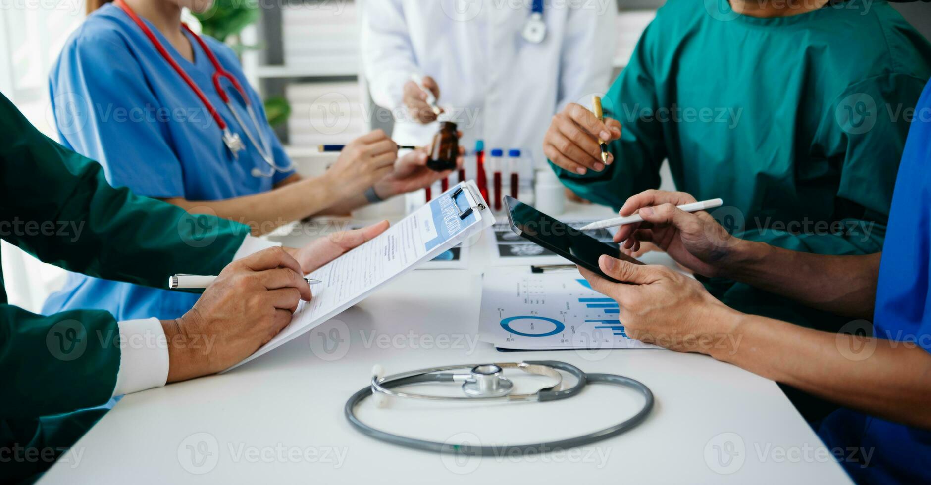 Medical team having a meeting with doctors in white lab coats and surgical scrubs seated at a table discussing a patients working online using computers in the medical industry photo