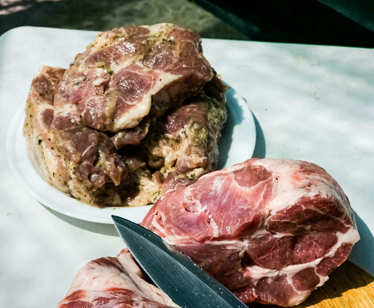 Fresh pieces of pork neck on a wooden kitchen board and marinated steaks on a plate. Pieces of pig meat close-up photo