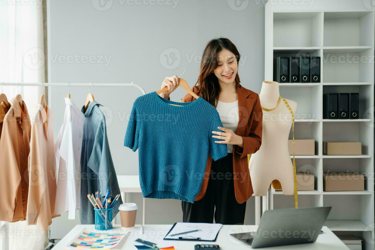 Successful fashion designer. Attractive young asian woman with smile while standing in workshop. Beautiful owner business woman working and holds tablet, laptop and smartphone in studio. photo