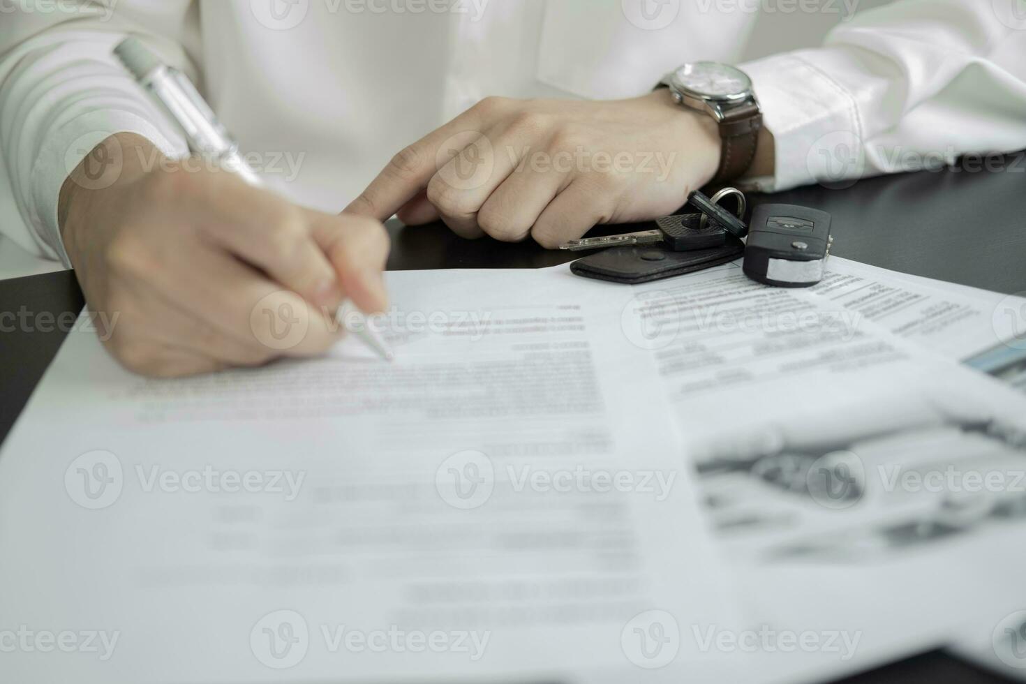 Man signing car insurance document or lease paper. Writing signature on contract or agreement. Buying or selling new or used vehicle. Car keys on wooden table. Warranty or guarantee. photo