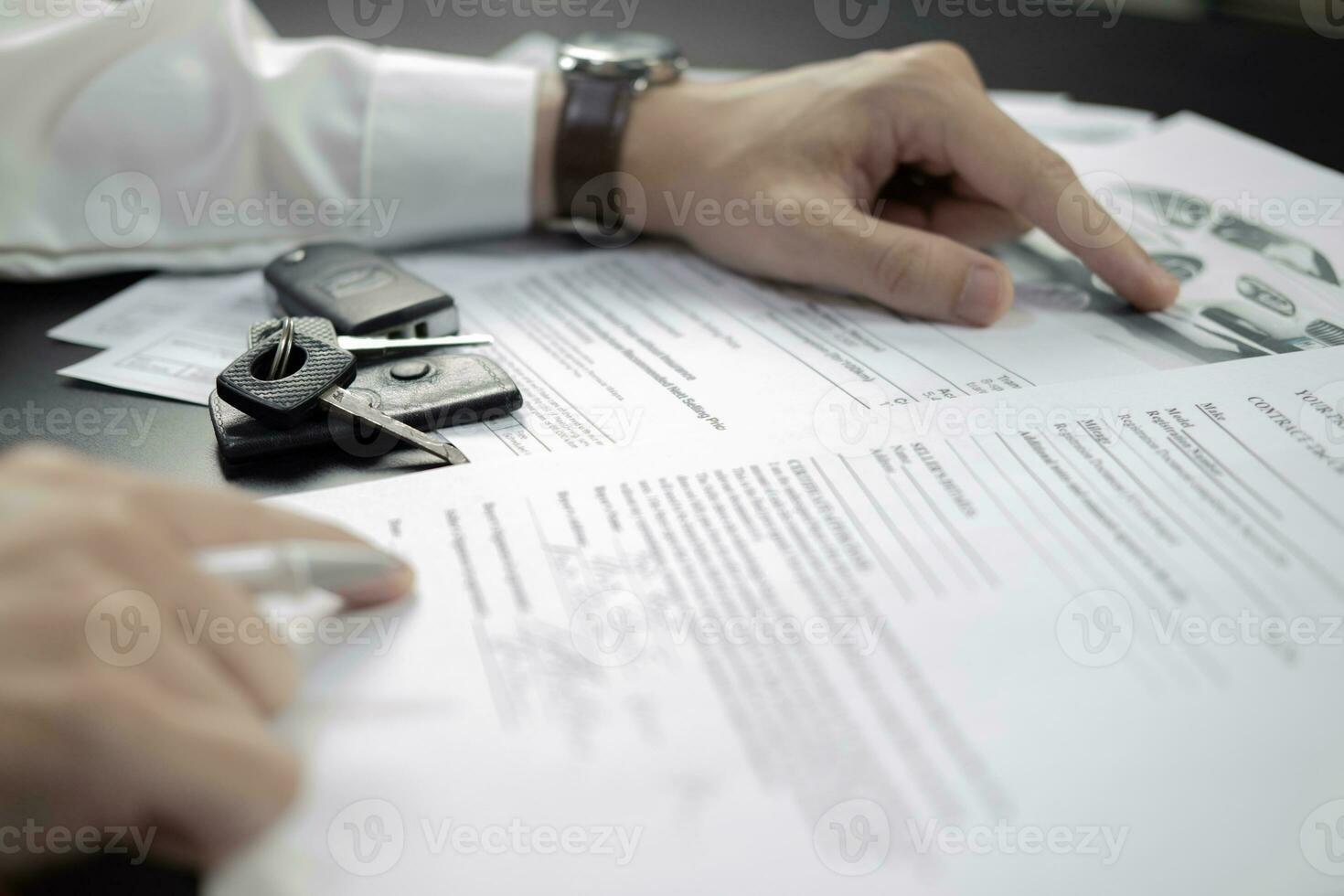 Man signing car insurance document or lease paper. Writing signature on contract or agreement. Buying or selling new or used vehicle. Car keys on wooden table. Warranty or guarantee. photo