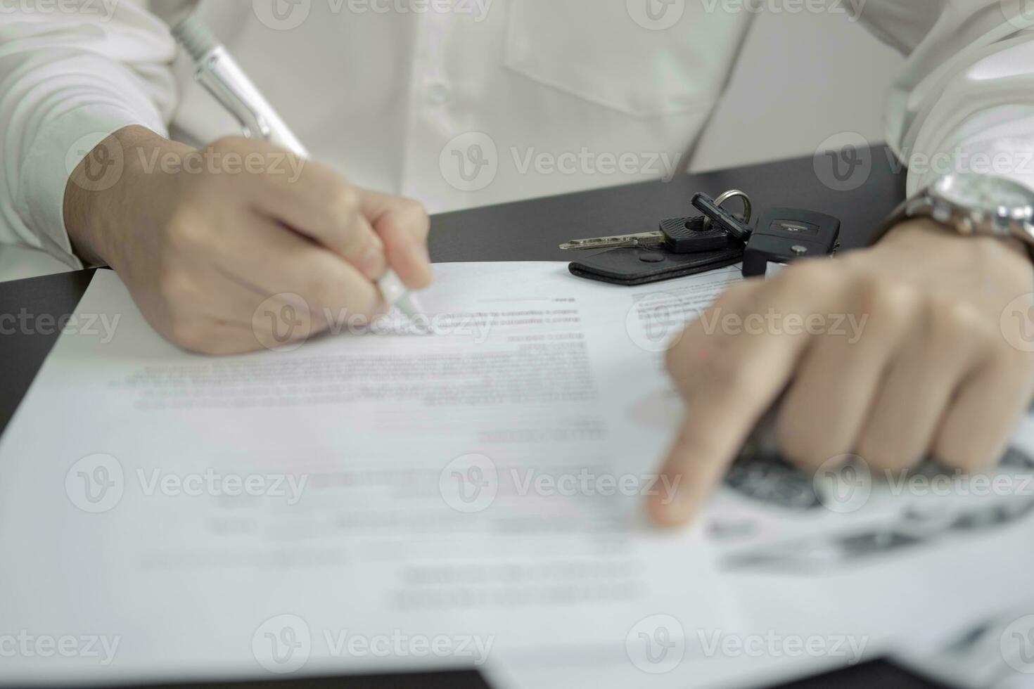 Man signing car insurance document or lease paper. Writing signature on contract or agreement. Buying or selling new or used vehicle. Car keys on wooden table. Warranty or guarantee. photo