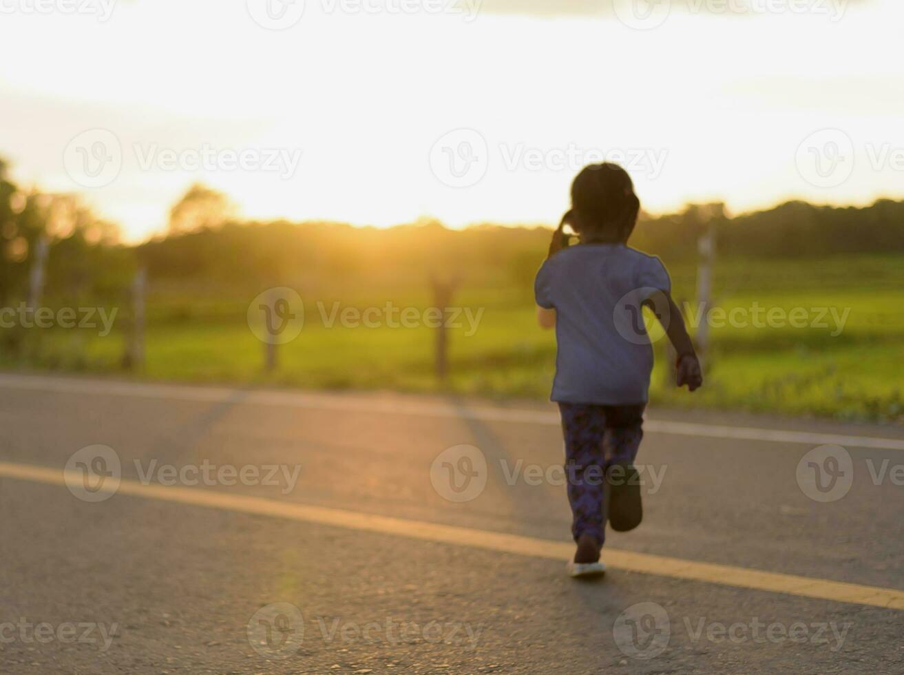 silueta de un contento niña corriendo a el la carretera en el dorado cielo a calentar amanecer en verano. foto