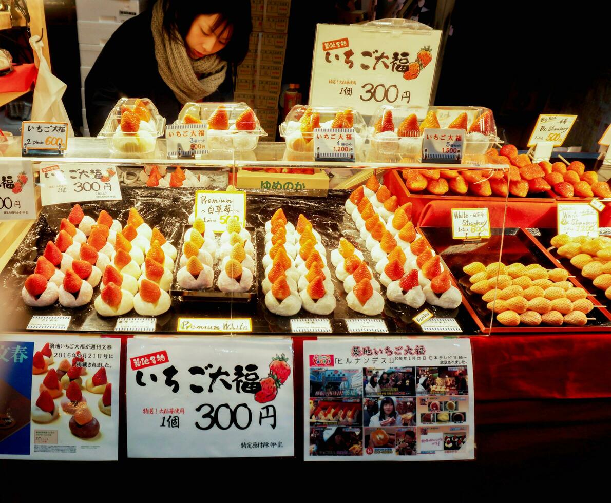 Osaka, Japan, 2018 - Big mochi filled with strawberries in a display cabinet with Japanese price and name labels. Colors and shapes inviting tourists to buy at the Kuromon Ichiba Market. photo