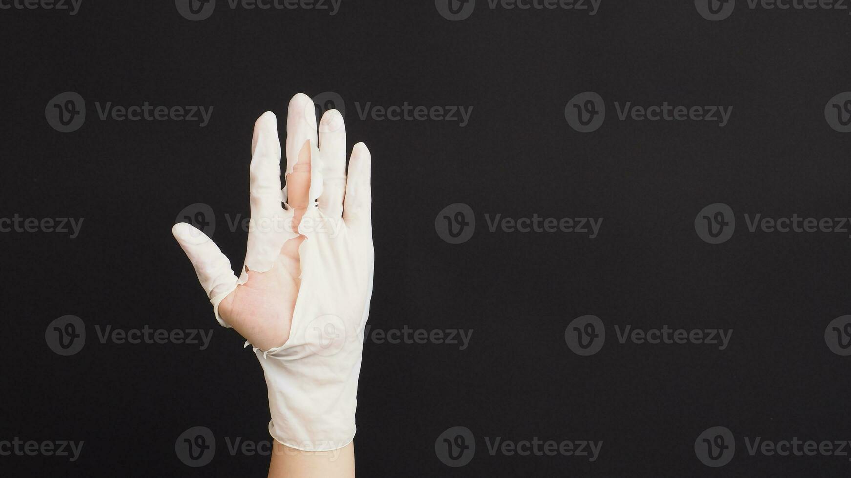 Hand Wearing torn latex glove or torn rubber gloves on black background. photo