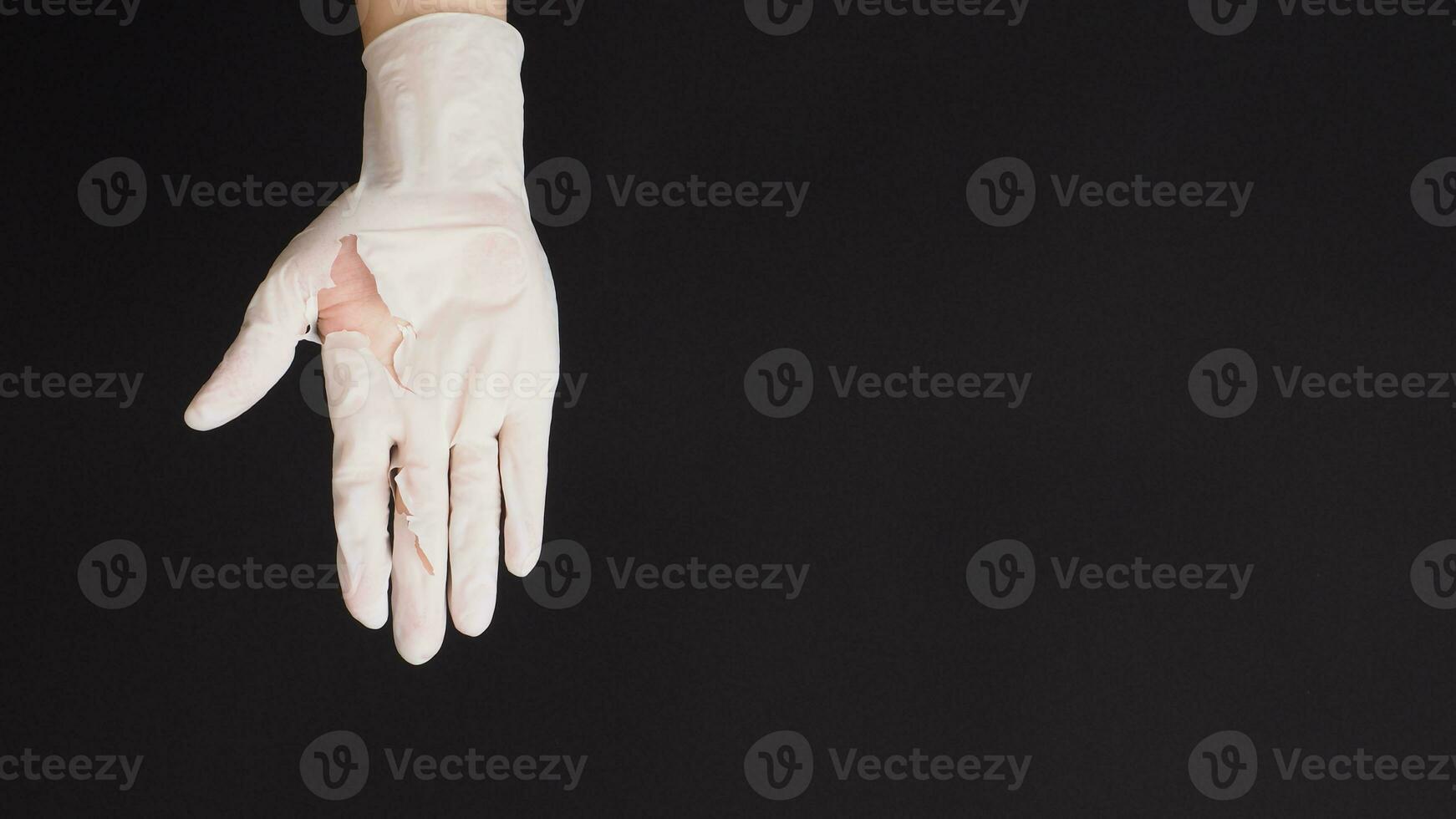Hand Wearing torn latex glove or torn rubber gloves on black background. photo
