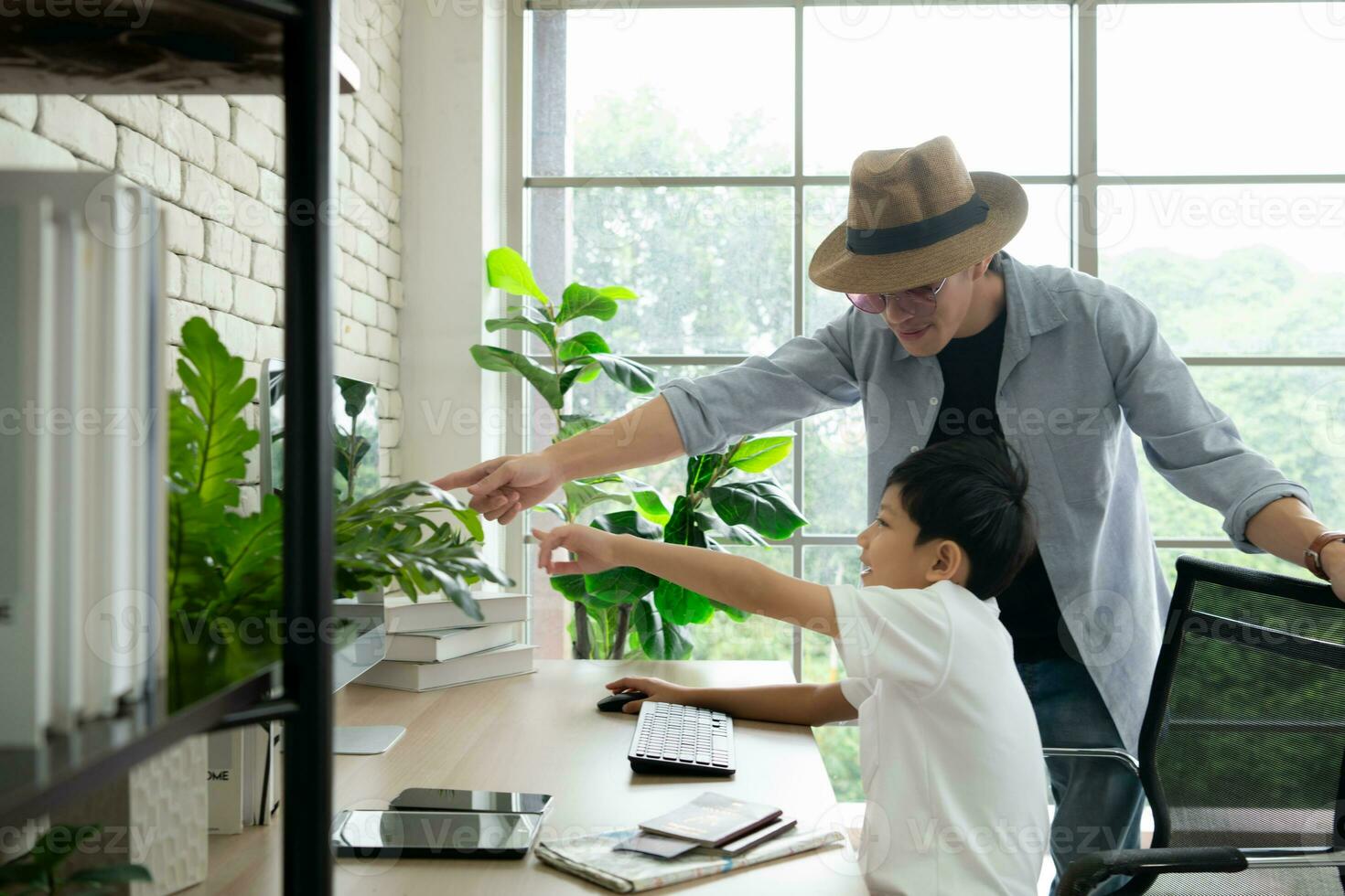 Son wearing headphones sits on computer desk chair with father, browsing for travel information for a weekend trip. photo