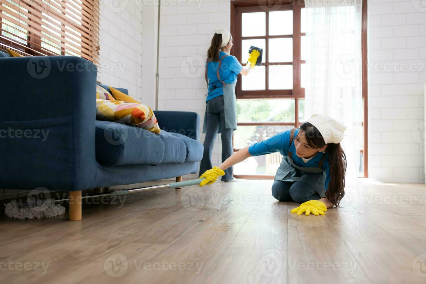 Two young women in uniform are cleaning the living room at home. photo