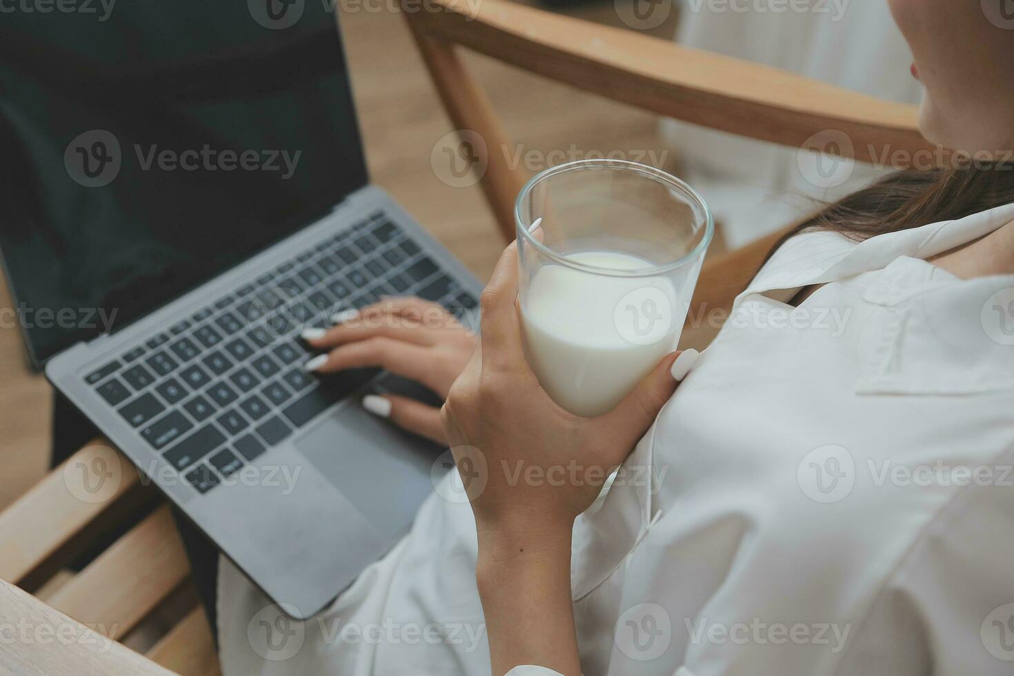 Happy young female in casual clothes smiling and looking at camera while using laptop on bed in bedroom at home photo