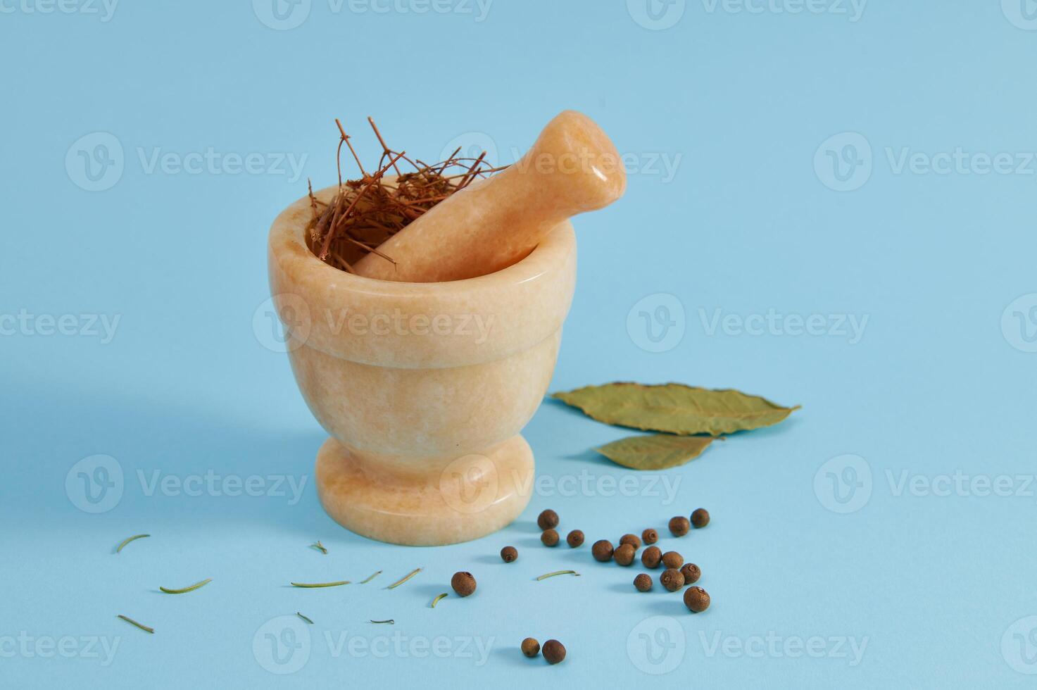 Beige marble mortar with pestle for grinding ingredients near peppercorns and bay leaf lying on a blue background with copy space. photo