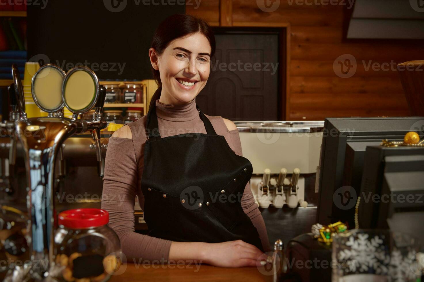 Young attractive smiling barista in apron standing behind the bar photo