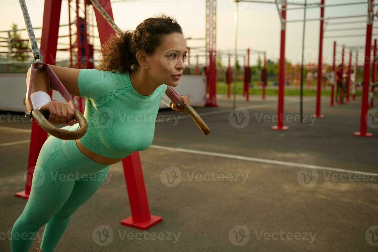 lado ver de joven atlético mujer con Perfecto cuerpo en ropa de deporte haciendo Lagartijas con aptitud suspensión correas en el campo deportivo. atractivo africano americano mujer trabajando fuera al aire libre a amanecer. foto