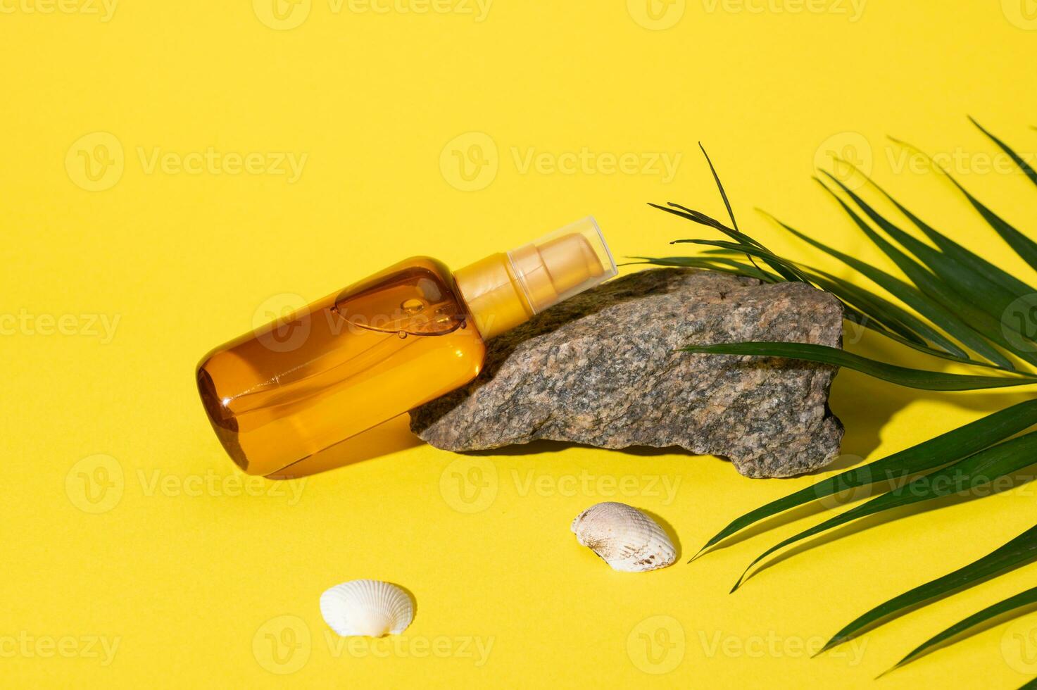 Still life with mockup bottle of sunscreen lotion on a small rock, sea shells and palm leaf, isolated yellow background. photo