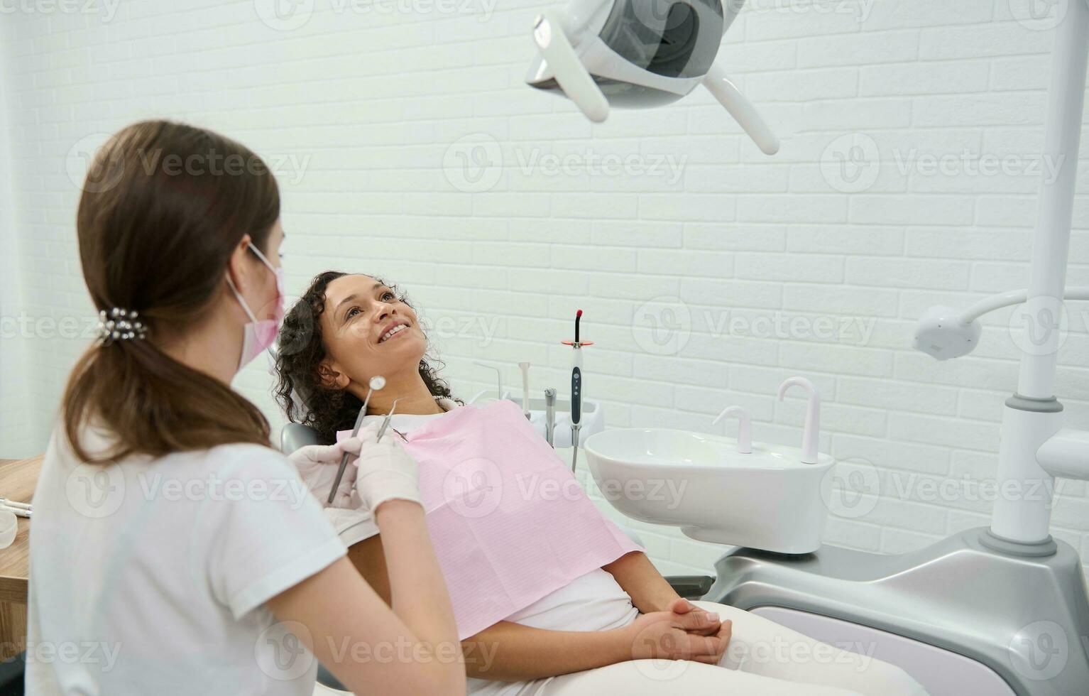 hermosa mujer en dentistas silla durante regular dental chequeo en moderno odontología clínica. oral higiene y dental cuidado, temprano diagnóstico de caries y dental enfermedades. salud cuidado, médico concepto foto