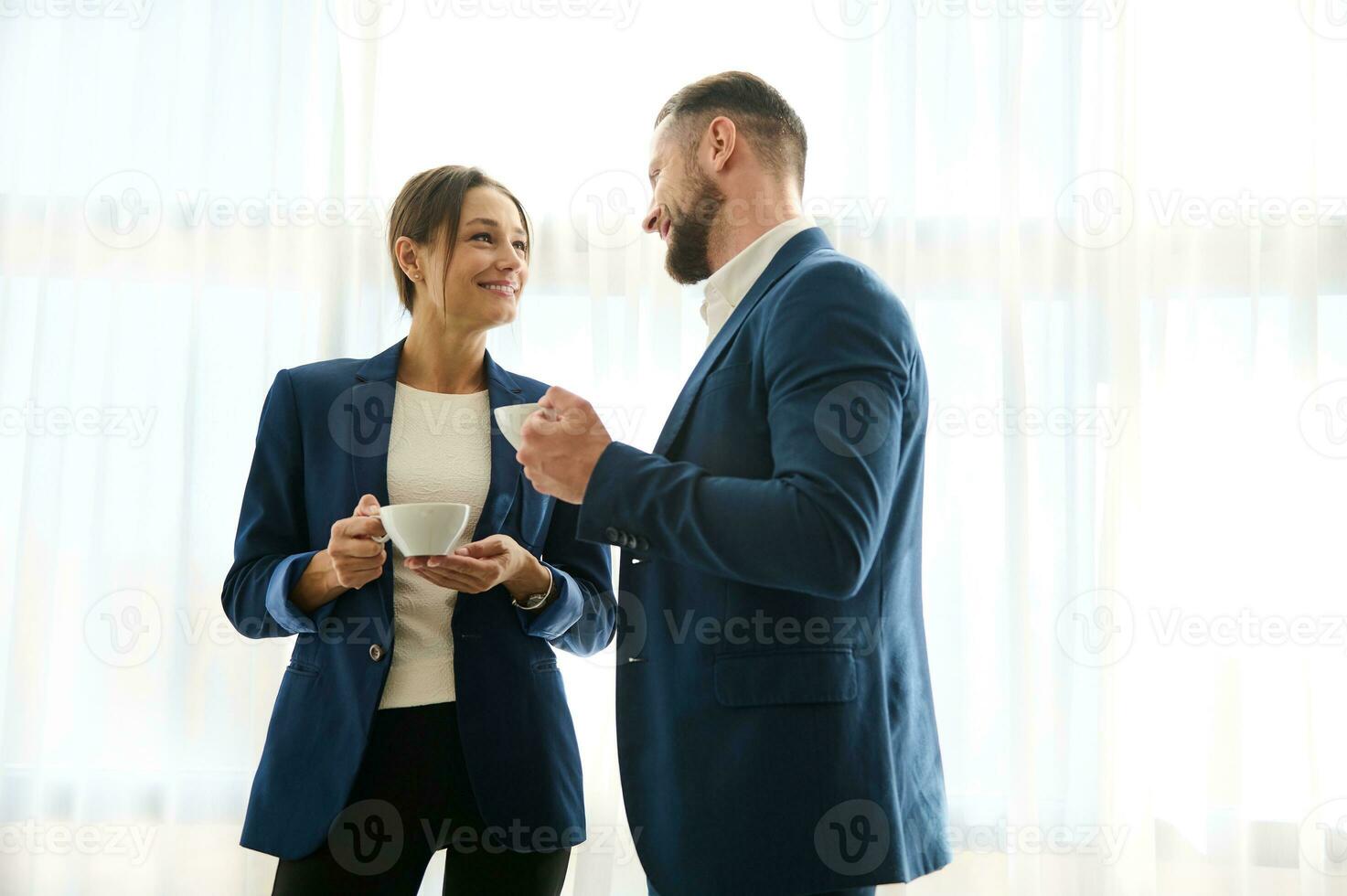 dos hermoso colegas, negocio socios, jefe y empleado flirteador juntos terminado un taza de café, en pie por el ventana en hotel habitación. intimidad amor asuntos a trabajar. compañero relación concepto foto