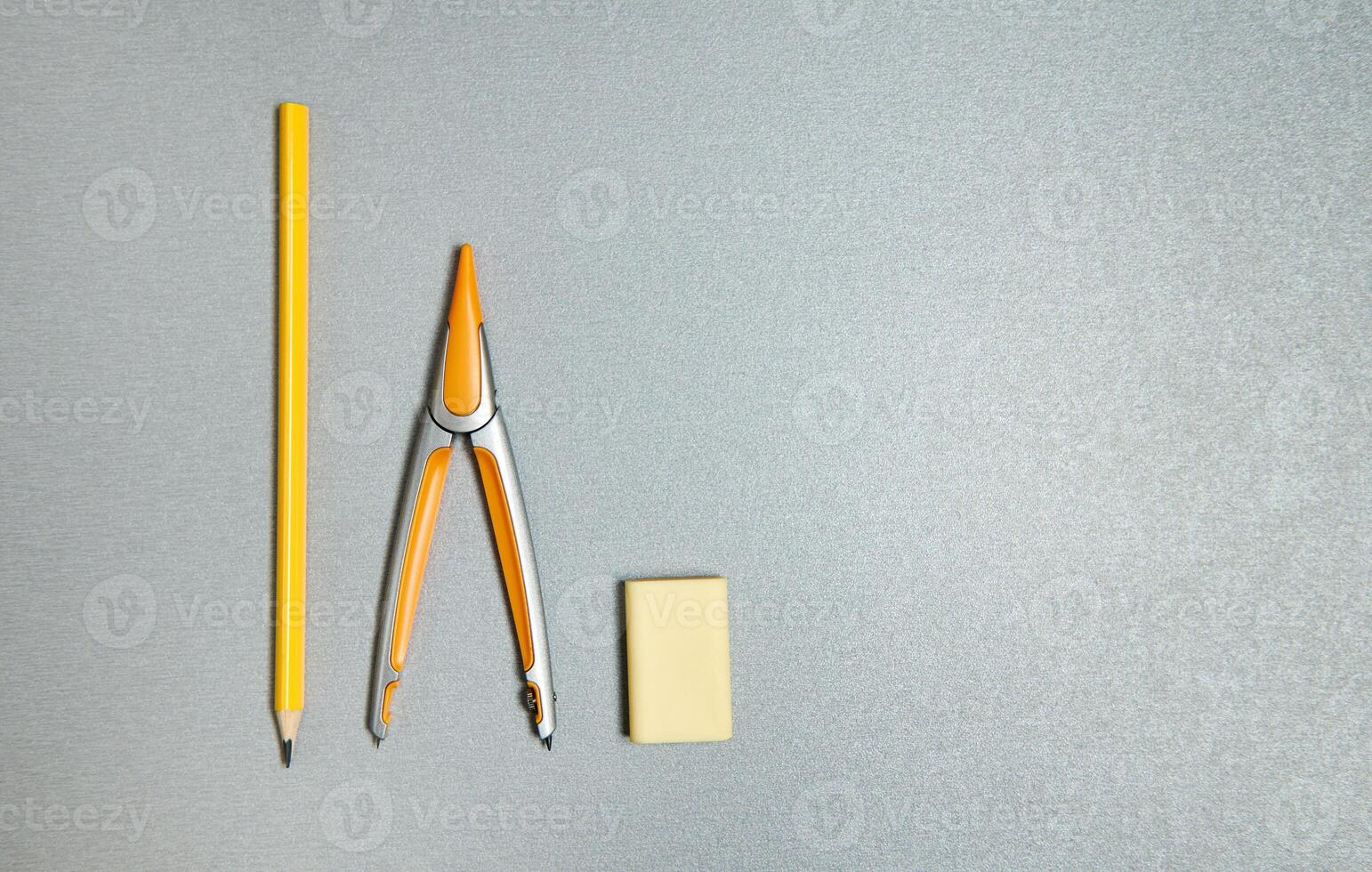 Pencil, eraser and compass. Flat lay composition of yellow office tools on a gray background. photo