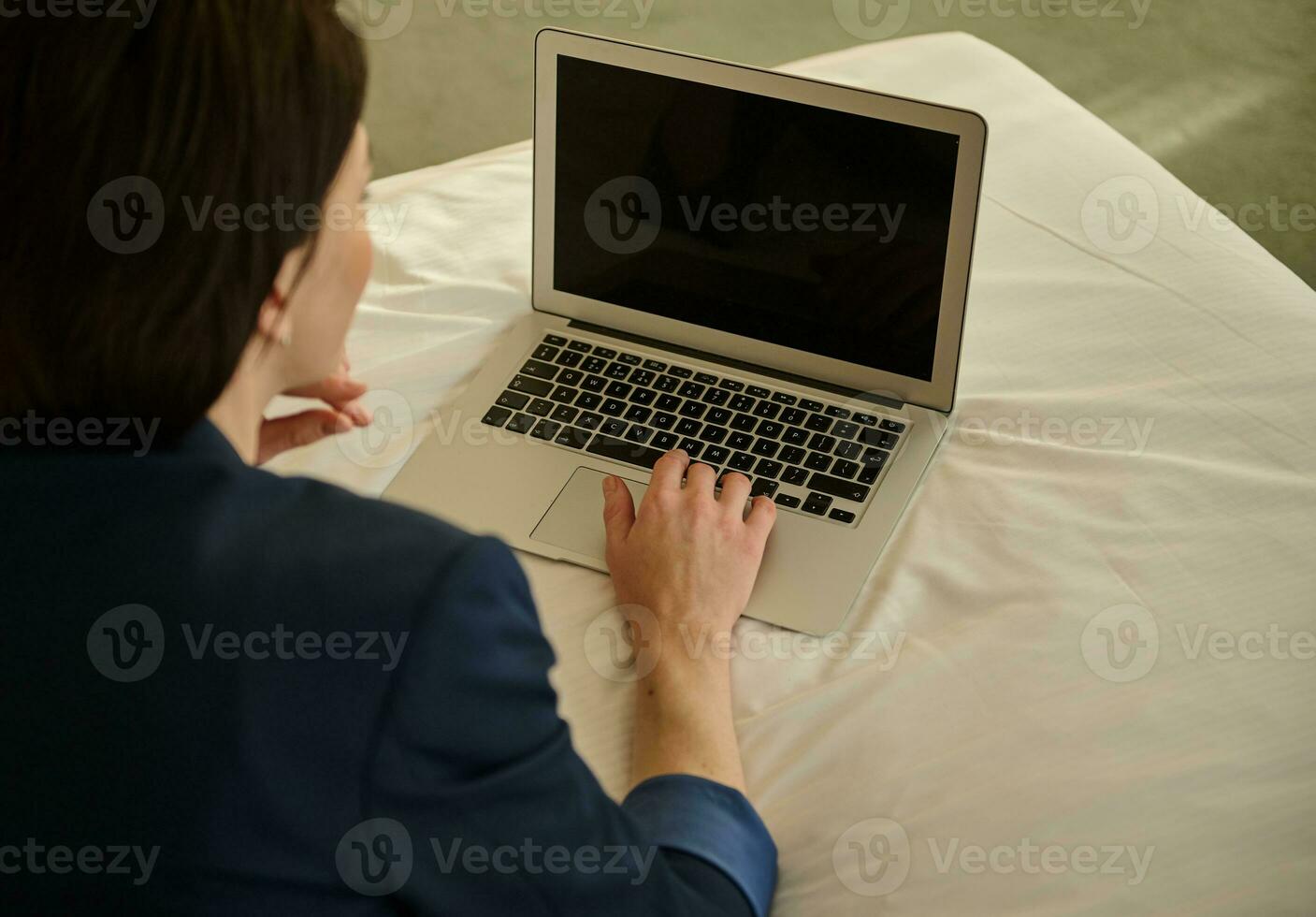 Focus on laptop with blank screen monitor. Overhead view of a businesswoman working on laptop, lying down on a bed photo