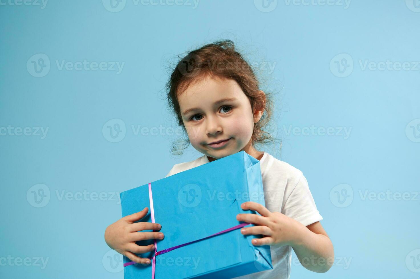 Adorable girl with blue gift on blue background with copy space. Children Day. Birthday concept. photo