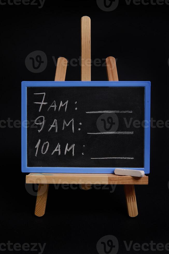 Lettering schedule with a white chalk, on a blackboard standing on a wooden table easel, isolated over black background with copy space. Planning concepts, time management, timetable and timing. photo