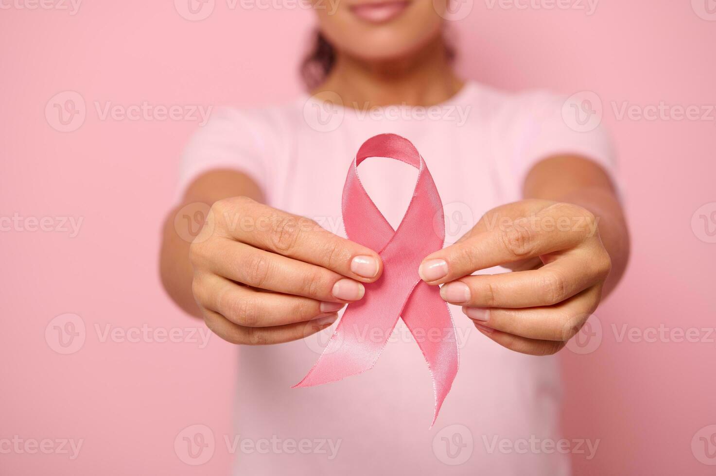 Cropped view of young woman in pink t-shirt holding a pink satin ribbon isolated on colored background with copy space. International Breast Cancer awareness Day, Breast cancer support concept. photo