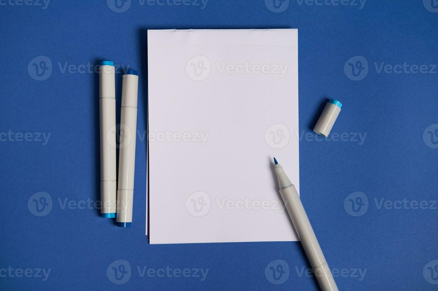 dicromático plano laico composición con acuarela marcadores o punta de fieltro plumas con un blanco blanco vacío papel sábana con Copiar espacio, aislado en azul antecedentes. foto