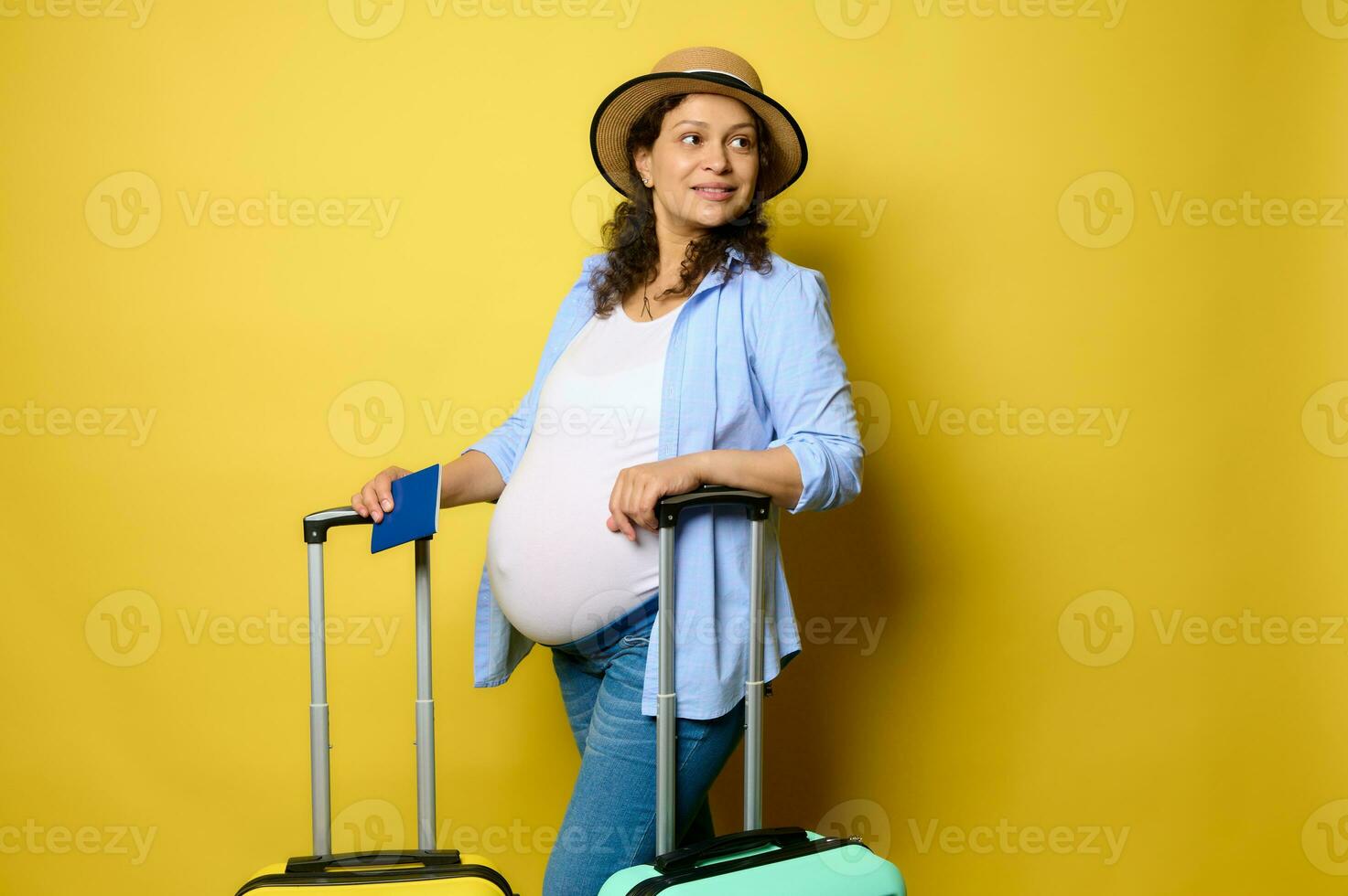 Smiling curly haired Latin pregnant woman going for summer getaway, travelling abroad, isolated yellow studio background photo