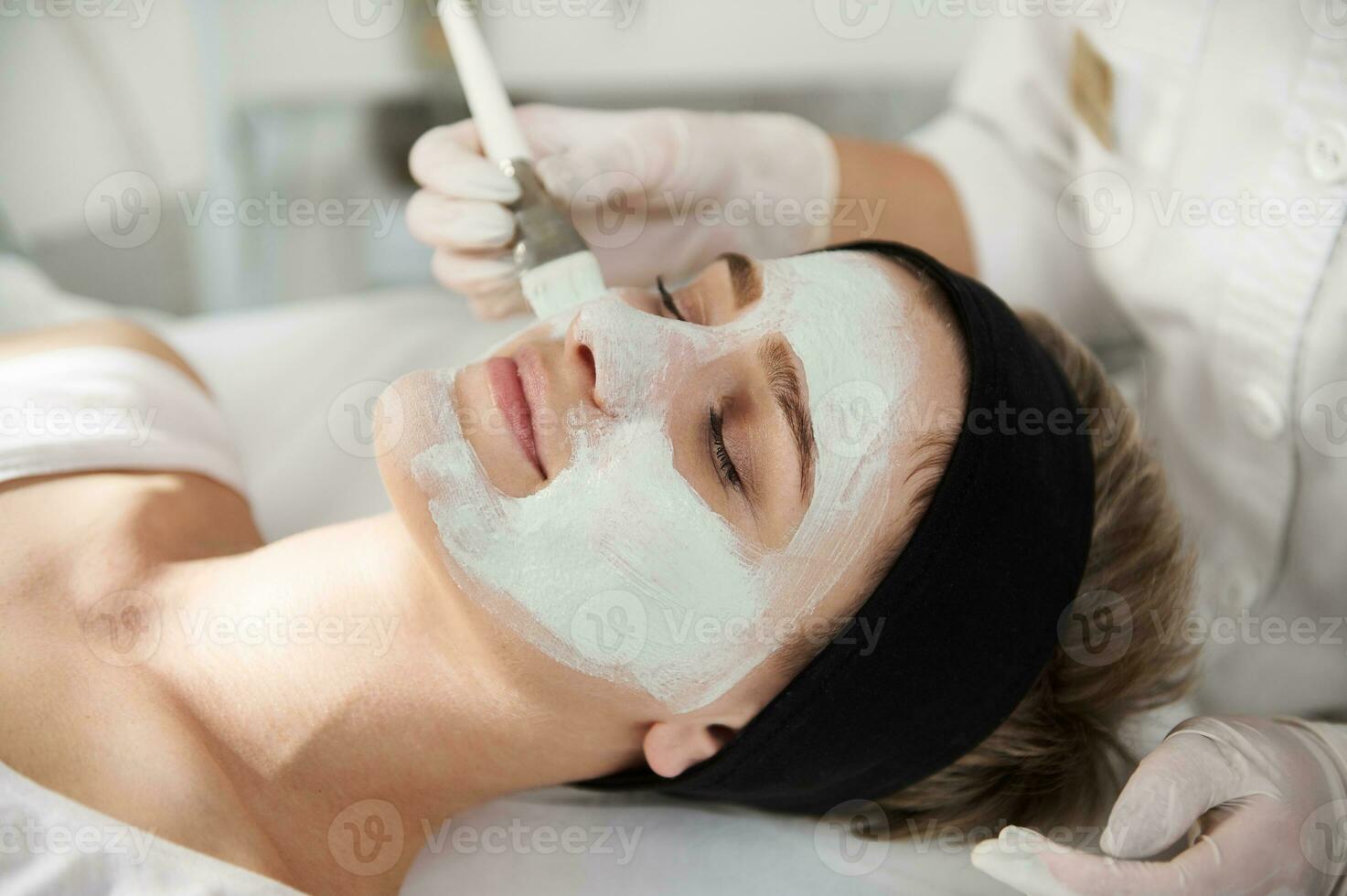 de cerca de cosmetóloga aplicando un algínico máscara en un hermosa mujer cara foto