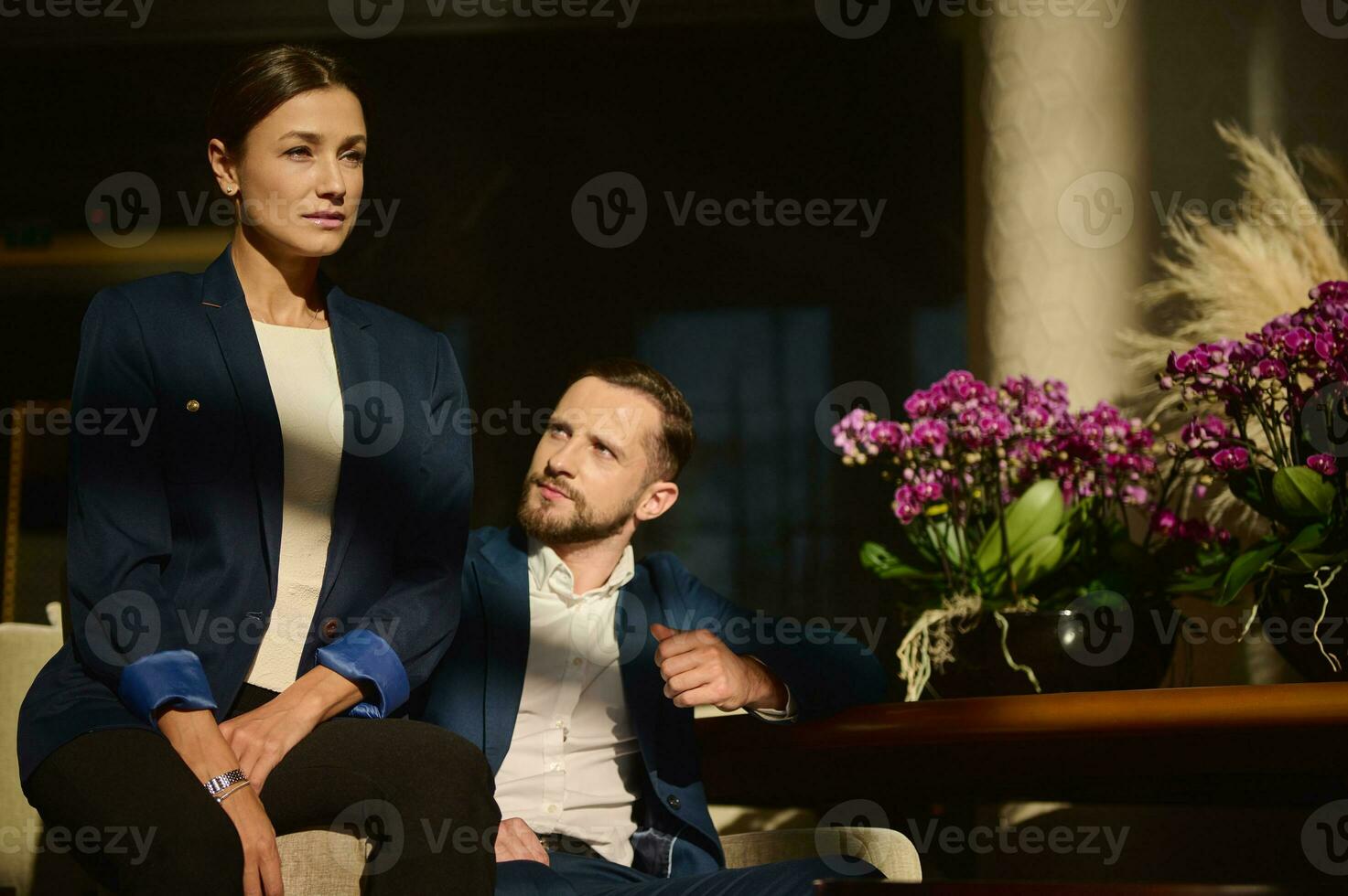 Portrait of two handsome confident people, colleagues on business trip, middle aged Caucasian woman and man , sitting on armchair in the lounge zone of a luxury hotel photo